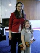 Kristin standing with a young violin student holding a small violin